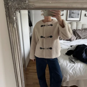 Beige teddyjacka med spännen - Säljer en beige teddyjacka med tre svarta spännen framtill. Från Gina i storlek M