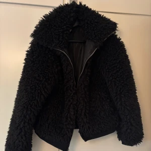 Svart teddyjacka från BikBok XS - Fluffig svart teddyjacka från BikBok i storlek XS. Jackan har en oversized krage, dragkedja framtill och är helfodrad. Perfekt för dig som vill ha en mysig och trendig look under kyliga dagar.