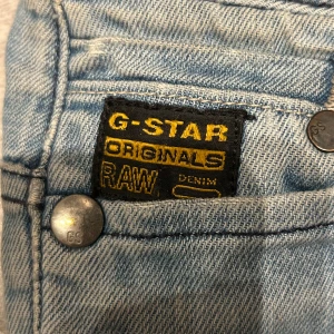 Ljusblå skinny jeans från G-Star RAW - Säljer ett par ljusblå skinny jeans från G-Star RAW med slitna detaljer och hål på båda knäna. Jeansen har klassisk femficksdesign, broderad logga bak och metallknappar med GS-märkning. Köpta för ca 1400kr säljer för 400kr.