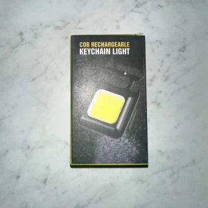 COB Rechargeable Keychain Light - Kompakt och uppladdningsbar nyckelringslampa med COB-floodlight, stark magnet, karbinhake och kapsylöppnare. Laddas via micro USB och har mini-format – perfekt för nyckelknippan eller väskan. Produkten är ny i förpackning och utan synliga skador.