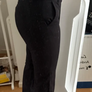 Svarta kostymbyxor från Gina Tricot - Säljer ett par svarta kostymbyxor från Gina Tricot i storlek 40. Byxorna har en klassisk rak passform med hög midja och vida ben. Perfekta för en clean och stilren look. Materialet känns mjukt och följsamt, och de har fickor i sidorna.