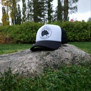 Svartvit truckerkeps AbbiCap Sweden - Snygg truckerkeps från AbbiCap Sweden i svart och vitt. Framsidan är vit med ett runt svart logomärke med pantermotiv, medan baksidan är i svart mesh för extra ventilation. Böjd skärm och justerbar passform. Perfekt för en cool och avslappnad stil.