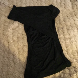 Svart offshoulder topp  - Säljer en svart, tight och offshoulder-topp i mjukt och stretchigt material. Toppen har en enkel och stilren design med smickrande passform och går som ett kors vid bysten, och är perfekt för dig som gillar minimalistisk stil. Snygg att styla med smycken eller boots.