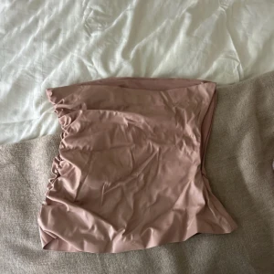 Rosa skinn från Zara - Säljer en ljusrosa topp från Zara i omlottmodell med snygga rynkade detaljer på sidorna. Toppen  har en tight passform och är gjord i ett mjukt syntetmaterial som känns skönt mot huden. Perfekt för dig som gillar trendiga och stilrena plagg.