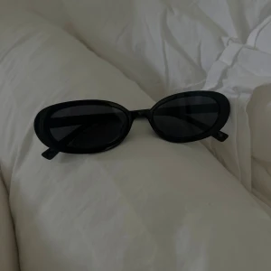 Svarta ovala solglasögon - Snygga svarta solglasögon med oval form och bred båge. Perfekta för att ge en cool vibe till din outfit. Glasen är mörka och ramen är i plast.