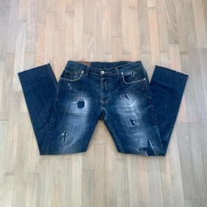 Dondup jeans - As snygga Dondupjeans med slitningar och hål på framsida och baksida. Jeansen har en unik stil längst ned! Bra skick förutom att det börjar bli slitet i skrevet dock ej synligt vid användning. Hör av dig vid minsta fundering!