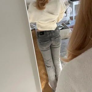 Gråa lågmidjade jeans från Replay - Säljer ett par gråa jeans från Replay med låg midja och raka ben. Jeansen har snygga slitningar, dubbla knappar i midjan och klassiska bakfickor. Perfekta för dig som gillar en avslappnad men ändå stilren look.