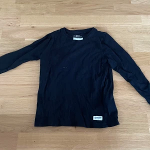 Svart långärmad tröja från 157 Denim Makers - En basic svart långärmad tröja från 157 Denim Makers. Tröjan har rund halsringning och en liten vit patch nertill med varumärket. Tillverkad i mjuk bomull, perfekt för lager-på-lager och chill vardagsstil.