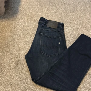 Replay Anbass mörkblå jeans - Snygga mörkblå Replay Anbass jeans med klassisk femficksdesign och diskret Replay-logga på bakfickan. Jeansen har en smal passform och är gjorda i stretchigt denim för extra komfort. Perfekta för dig som gillar stilrena och moderna jeans.