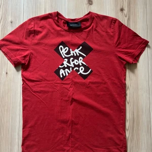 Röd Peak Performance t-shirt med tryck - M - Röd t-shirt från Peak Performance i bomull med coolt svart och vitt tryck framtill. Klassisk rund hals och korta ärmar. Perfekt för dig som gillar streetstyle och vill sticka ut med en snygg grafisk detalj.