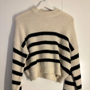 Randig stickad tröja i beige och svart - Säljer en chunky stickad tröja i beige med svarta ränder från Nelly. Den är lite nopprig men inget jag har tänkt på när jag använt den.