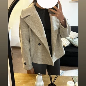   Höst/vinter jacka/kappa - Snygg kort kavaj i ljus grå med svarta knappar framtill och vid ärmslut. Jackan är oversize passform, beställde M men den är mer L. Inte använd något endast testad. Den är fin till hösten och våren lite för tunn för vintern (i min åsikt💕)