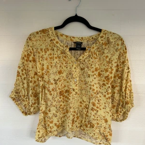 Gul blommig blus - Söt blommig blus från Lindex i storlek XS. Blusen är ljusgul med små bruna blommor, har trekvartsärmar med resår och knappar framtill. Luftig och flowy passform, perfekt för vår och sommar. Tillverkad i mjuk bomull.🤩💕