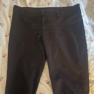 Svarta kostymbyxor bootcut  - Snygga svarta kostymbyxor med bootcut och två knappar i midjan. Klassisk passform och stilren look, perfekta till en dressad outfit. Byxorna har diskreta fickor och är tillverkade i ett mjukt tyg som känns bekvämt hela dagen.