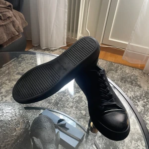 Svarta sneakers från Sneaky Steve - Snygga helsvarta sneakers från Sneaky Steve med ovandel i mocka och tåparti i slätt skinn. Skorna har klassisk snörning och platt sula, perfekt för en clean och stilren look. Passar dig som gillar minimalistisk design och svart på svart. Pris ej hugget i sten