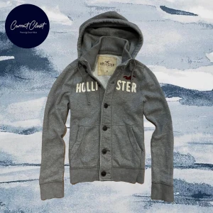 Grå hoodie/ cardigan med knappar från Hollister - Grå hoodie från Hollister med broderad logga och text på bröstet | Size M | Vintage och otroligt limiterad!! | Längd: 68cm Axelbredd: 40cm