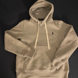  Polo Ralph Lauren hoodie - Snygg grå hoodie från Polo Ralph Lauren med klassisk broderad logga på bröstet. Tröjan har huva med snörning, känguruficka och ribbade muddar. Perfekt för en chill och stilren look. Den är använd 2-4 gånger helt ny den blev för liten kan snacka om priset. 