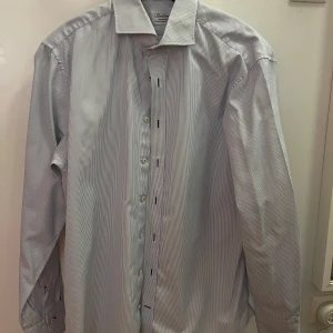 Randig skjorta från Stenströms, strl 41 - Klassisk skjorta från Stenströms i vit och ljusblå randigt mönster. Skjortan har lång ärm, knappar framtill och en snygg krage. Tillverkad i exklusiv tvåfaldig bomull för en mjuk och lyxig känsla.