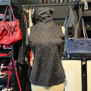 Glittrig svart polotopp  - Svart ärmlös polotopp från Alyssa Michele med glittrigt lurex-tyg. Toppen har en hög polokrage och är tillverkad i stretchig polyesterblandning. Perfekt för dig som vill sticka ut med en cool och trendig look.