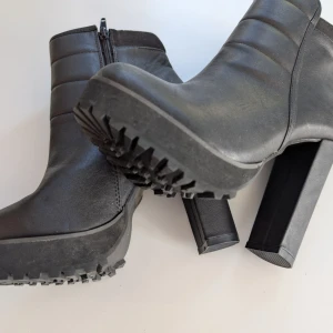 Helt nya! Svarta stövletter med klack från NLY Shoes - Snygga svarta stövletter från NLY Shoes med chunky hög klack och grov sula. Skorna är i syntetmaterial med dragkedja på sidan och quiltade detaljer upptill. Perfekta för dig som vill ha en edgy look med extra höjd.