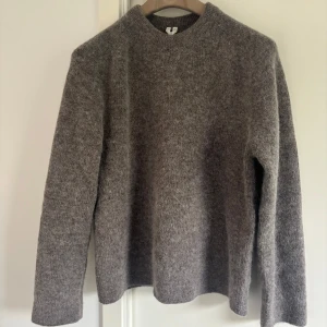Arket grå ulltröja - Säljer en stilren grå stickad tröja från arket i mjuk alpacka ull. Tröjan har rund hals, lång ärm och en loose passform som ger en chill vibe. Perfekt för dig som gillar klassisk design med lyxig känsla.