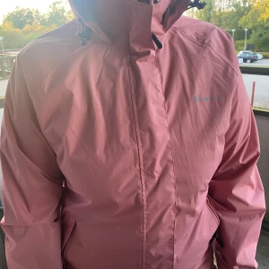 Rosa vindjacka från Trekmates, stl L - Säljer en snygg rosa vindjacka från Trekmates i storlek L. Jackan har huva med dragsko, dragkedja framtill och meshfoder på insidan för extra komfort. Perfekt för blåsiga dagar och outdoor-äventyr.