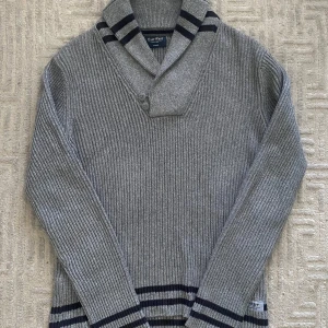 Grå cardigan från East West - Ribbstickad grå tröja från East West i 100% bomull. Snygg krage med två knappar och mörkblå ränder på krage och nederkant. Långärmad och perfekt för kyligare dagar. Storlek M och passar TTS, vid fler frågor eller funderingar tveka inte på att skriva till mig!