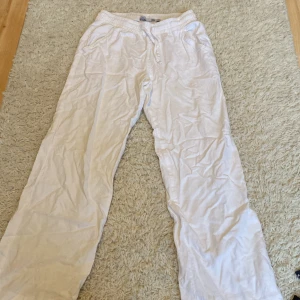 Vita linnebyxor med snörning 157 - Vita linnebyxor från 157 med avslappnad passform och resår i midjan samt snörning. Byxorna har raka ben och fickor både fram och bak. Perfekta för en chill och luftig stil under varmare dagar.