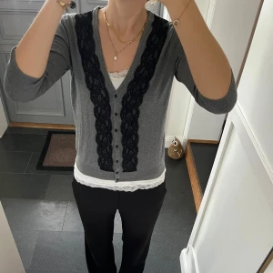 Grå stickad kofta  - Trekvartsärmad stickad kofta med svart spets från H&M i storlek S. Fint skick. Använd gärna köp nu!