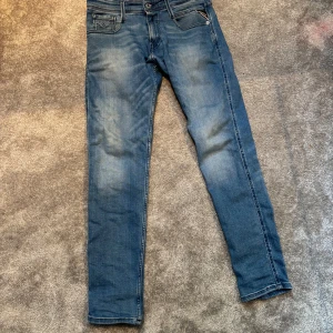 Replay Anbass blå jeans slim fit - Snygga ljusblå Replay Anbass jeans i slim fit med klassisk femficksdesign och diskreta slitningar. Jeansen har normal midja och raka ben, tillverkade i mjukt bomullsmaterial med lite stretch för extra komfort. Perfekta för en avslappnad och trendig look. Nästan oanvända