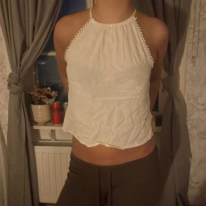 Vit ärmlös linnetopp med pärldetaljer - Säljer en vit ärmlös linnetopp med tunna axelband och pärldetaljer längs kanterna. Toppen har en lös passform och lätt rynkad textur, perfekt för varma dagar. Enkel och stilren design som passar till många outfits.