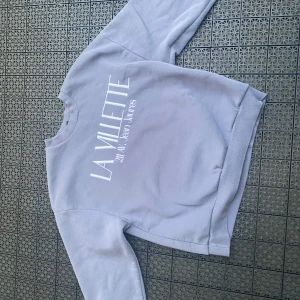 Grå sweatshirt från Gina Tricot - Säljer en grå sweatshirt från Gina Tricot med broderad vit text 'LA VILLETTE 211 AV. Jean Jaures' på bröstet. Tröjan har rund hals, långa ärmar och är i mjuk bomullsblandning. Perfekt för chill dagar eller när du vill ha en clean look.