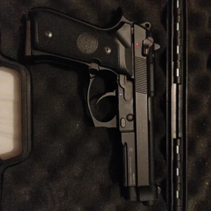 M9 6mm baretta Airsoft pistol - Bilderna visar en Beretta M9/92FS-liknande pistol med magasin, förvarad i vadderat fodral. Pistolen har märkning 'U.S. M9 ARMED FORCES' och Beretta-logga på greppet Material metall fylls på med gas i Magasinet skickar med en gastub som e halv full. Pistolen är aldrig använd. Skriv vid intresse/ vill ha mer bilder på pistolen. Ny pris 1400kr. Den tar 6 mm kulor i maget 👍
