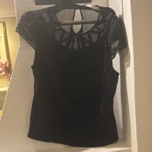 Svart meshblus från Karen Millen - Säljer en svart blus från Karen Millen med transparent mesh upptill och på ärmarna. Blusen har ett unikt geometriskt mönster vid halsringningen och korta ärmar. Perfekt för dig som gillar stilrena detaljer och snygg design.