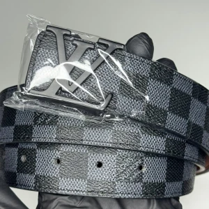 Louis Vuitton rutig svart bälte - Snyggt bälte från Louis Vuitton med klassiskt rutigt mönster i svart och grått. Bältet har en stor LV-logga i metall som spänne och är tillverkat i skinn. Perfekt för att lyfta din outfit med en exklusiv touch.