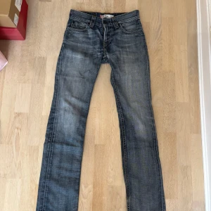 Levi's 511 blå jeans straight fit - Säljer ett par klassiska Levi's 511 jeans i blå tvätt med snyggt slitna detaljer. Modellen har rak passform, fem fickor och guldfärgade sömmar. Jeansen är tillverkade i bomull och har den ikoniska läderpatchen bak i midjan. Storlek 30/34!🩷