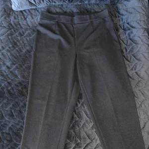 Svarta kostymbyxor  - Snygga svarta kostymbyxor med klassiskt snitt och pressveck framtill. Byxorna har en rak passform och bred linning, perfekta för en clean och stilren look. Passar dig som gillar enkel och tidlös stil. Korta i passform.