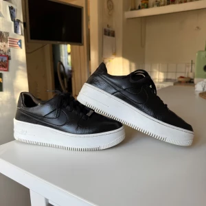 Nike Air Force 1 Sage Low svart/vit - Säljer ett par Nike Air Force 1 Sage Low i svart skinn med chunky vit plattformssula. Klassisk Swoosh-logga på sidorna och snörning framtill. Något creasade på vänster sko och lite slitna under sulan, men sparsamt använda