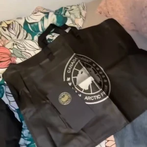 Svart dunjacka med päls från Canada Goose - Säljer en svart dunjacka från Canada Goose med ikonisk röd logga på ärmen och fluffig beige päls runt huvan. Jackan har dragkedja och knappar framtill, samt en klassisk puffer-design som håller dig varm under vintern. Perfekt för dig som vill ha både stil och funktion. Priset kan diskuteras dm ba kan ge skit mycke rabbat