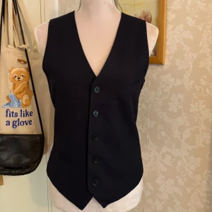 Marinblå kostymväst från H&M Slim Fit - Stilren marinblå kostymväst från H&M i herrstorlek 44 slim fit-modell. Västen har fyra knappar framtill, v-ringning, fickor och justerbart spänne i ryggen. Perfekt till hösten när man vill börja ha på sig flera lager. 