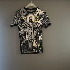 Brasilien Neymar Jr 10 fotbollströja - Unik svart fotbollströja med Neymar Jr och nummer 10 på ryggen. Framsidan har ett detaljerat,med Kristusstatyn, brasilianska flaggan och coola grafiska detaljer i svart, vitt och gult. Korta ärmar och sportig passform, perfekt för dig som älskar Brasilien och fotboll.