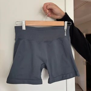 Mörkgrå träningstights-shorts från DFYNE - Snygga mörkgrå shorts från DFYNE med hög midja och tight passform. Tillverkade i ett stretchigt syntetmaterial som sitter skönt vid träning. Ribbad linning och diskret logga framtill och baktill. Perfekta för gymmet eller löprundan. Modellen Impakt