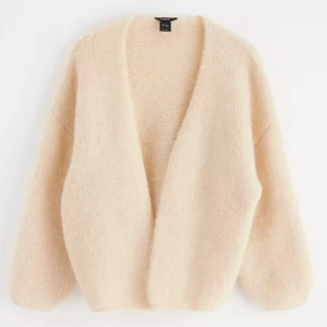 Beige stickad kofta från lindex - Supermjuk och fluffig beige kofta från  Lindex . Koftan är stickad, har en djup v-ringning och ballongärmar för en chill och oversized vibe. Perfekt att slänga över en t-shirt eller klänning när det är lite kyligt ute.