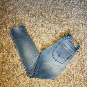 Replay anbass Ljusblå  jeans med slitning - Replay anbass jeans i ljusblå tvätt med klassisk femficksdesign och snygga slitningar. Jeansen har raka ben och slim passform, med en diskret slitning på ena benet. Storlek 32/32, postas antigen samma dag som köp eller dagen därpå, sänker priset 50 kr vid snabb o smidig affär💯🙌
