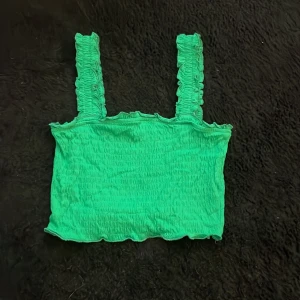 Grön smockad linnetopp Vero Moda XS - Superfin grön smockad linnetopp från Vero Moda i storlek XS. Toppen har breda, rynkade axelband och en croppad passform med vågig kant nertill.💚