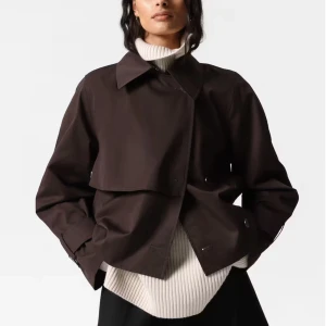 Brun kort trenchcoat & other stories  - Snygg oanvänd kort trenchcoat i mörkbrunt storlek S  köpte den för 1590kr .med klassisk krage och knappar framtill. Jackan har breda ärmar med spänndetaljer vid handlederna och en oversized passform. Perfekt för lager-på-lager och ger en cool, stilren vibe. Kvittot finns är tyvärr stor på mig 