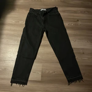 Svarta jeans från Bershka med fransad kant.  Strl 36 - Svarta jeans från Bershka i rak modell med snygga fransade benslut. Klassisk femficksdesign och normal passform. Perfekta för dig som gillar en stilren look med en twist. Jeansen är tillverkade i ett mjukt bomullsmaterial.