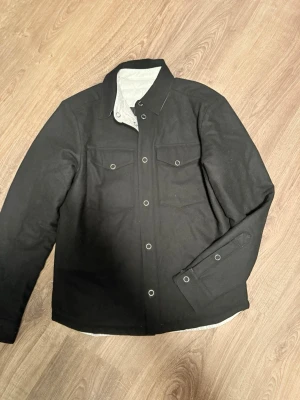 J Lindberg overshirt/jacka  - Jacka från J Lindberg i strl M, den går att vända ut och in ifall man föredrar den vita looken. Köpt i deras butik och varan är i bra skick.
