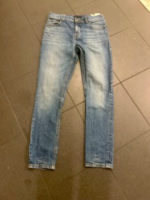 Tommy Hilfiger Blå raka jeansbyxor stl 152 - Säljer ett par klassiska blå jeansbyxor med raka ben och fem fickor. Jeansen har en ljus tvätt med slitningar och normal passform. Perfekta till vardags och lätta att matcha med olika stilar.