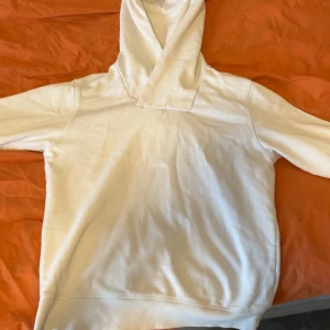 Vit hoodie med huva - Klassisk vit hoodie med huva och lång ärm. Hoodien har en enkel och clean design utan synliga loggor eller tryck. Perfekt för en avslappnad och stilren look. Tillverkad i mjukt material för extra komfort.